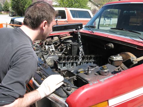 1981 Ford Bronco - Man works on the engine of a red 1981 Ford Bronco, with another Bronco visible behind.
