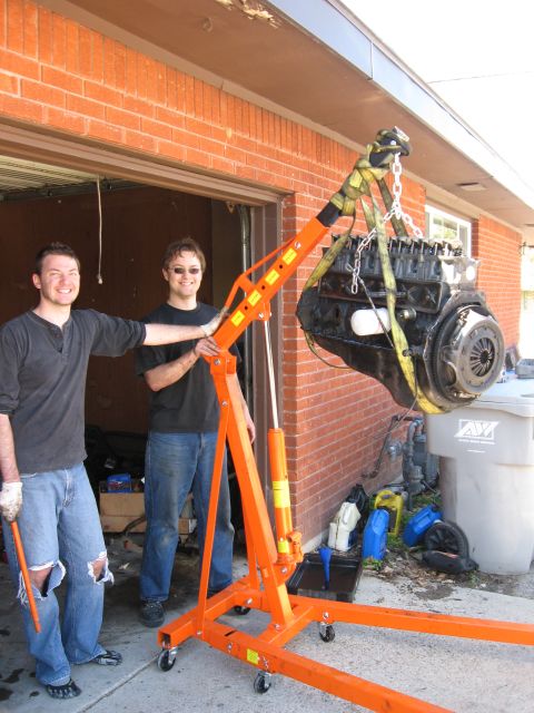 1981 Ford Bronco - Engine hoist lifting a black engine block with two men nearby.