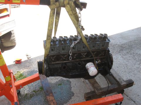 1981 Ford Bronco - An engine is suspended by straps and chains from an engine hoist, ready for installation or removal.