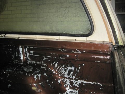 1979 Ford Bronco - The interior of a pickup truck bed is shown, a white camper shell window and brown metal sides with white residue.