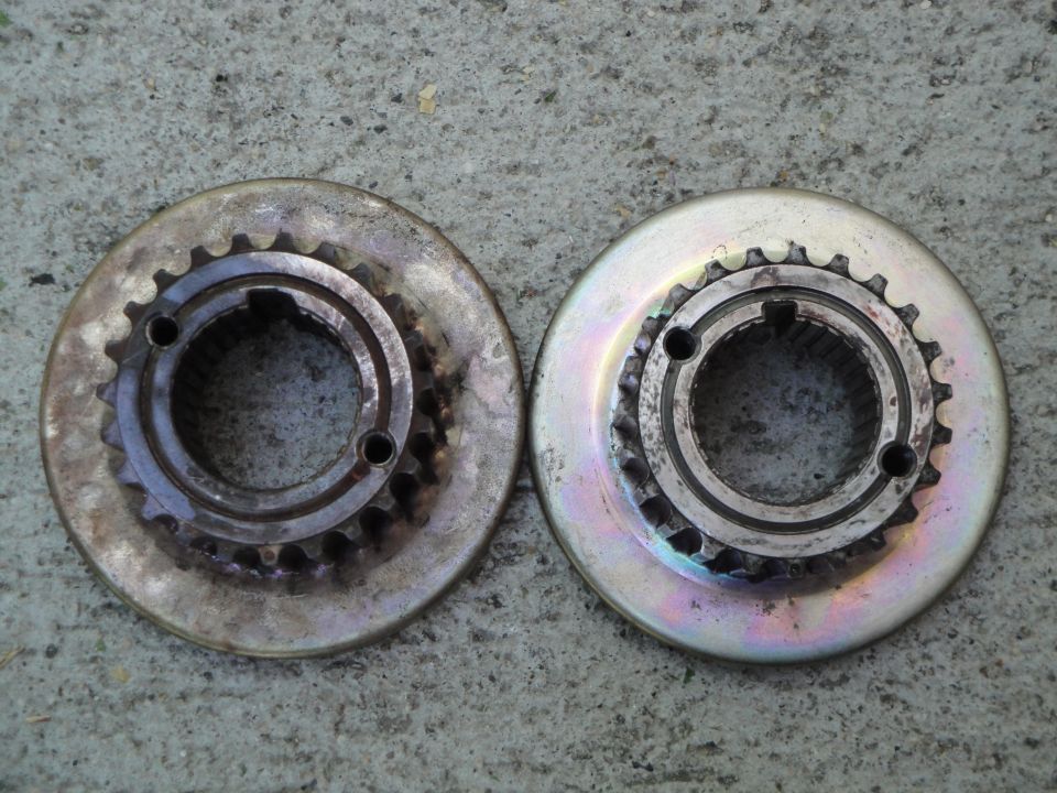 Two metal sprockets with splined centers sit on a concrete surface