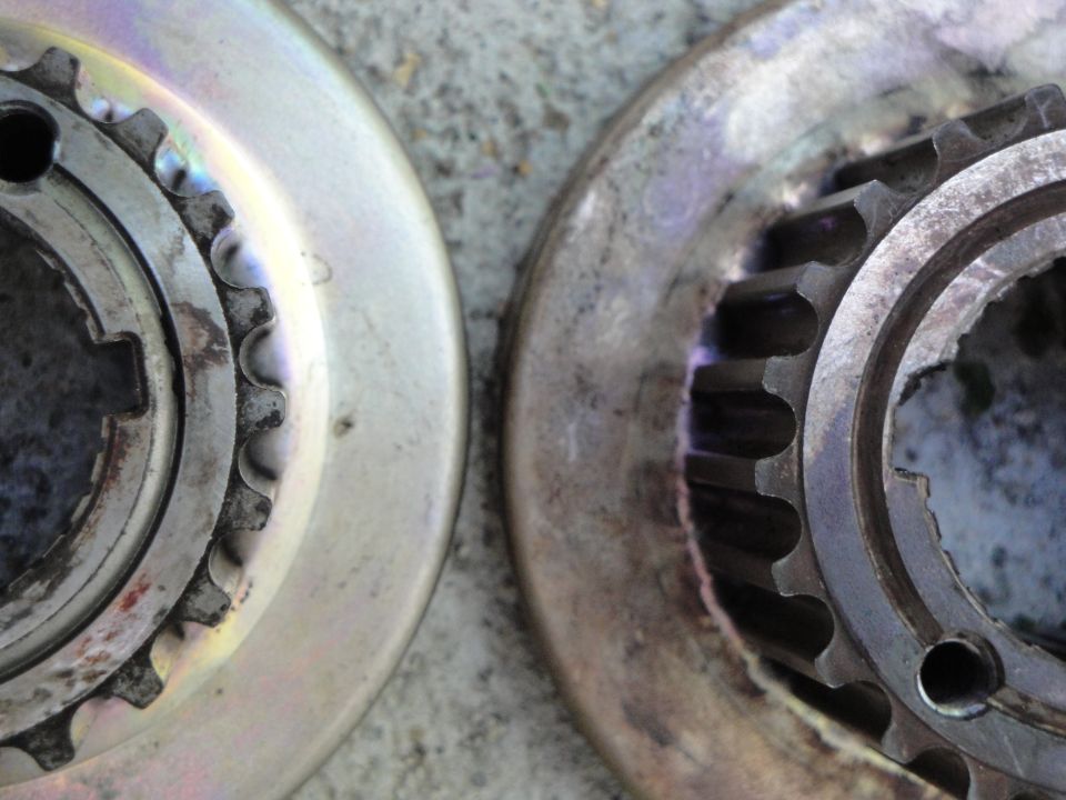 Two metal sprockets with teeth, one lighter and one darker, on a textured surface