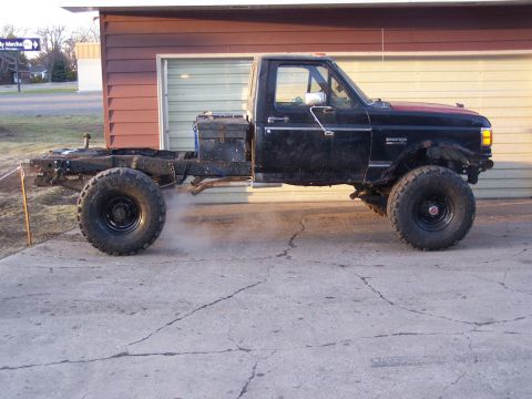 1988 Ford F-250 - This modified pickup truck, likely a 1987 model, is shown from the side, stripped down to its chassis and large off-road tires.