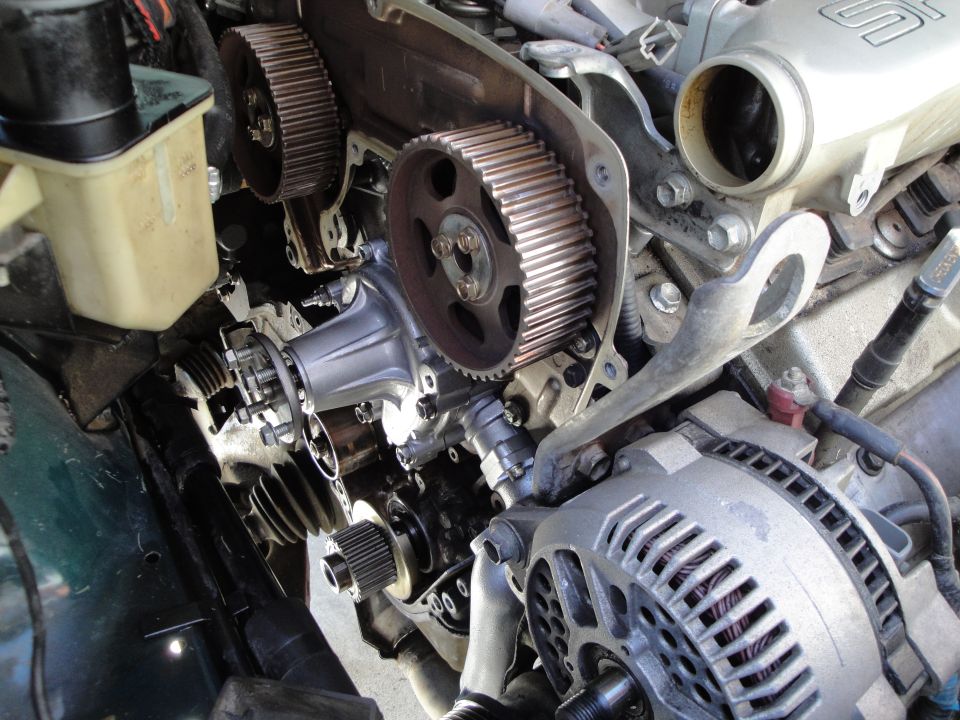 Engine timing belt and water pump assembly with alternator. Green car fender visible