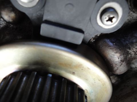 1995 Ford Taurus - Close-up of a crankshaft position sensor positioned near a toothed wheel, likely part of an engine's timing system.