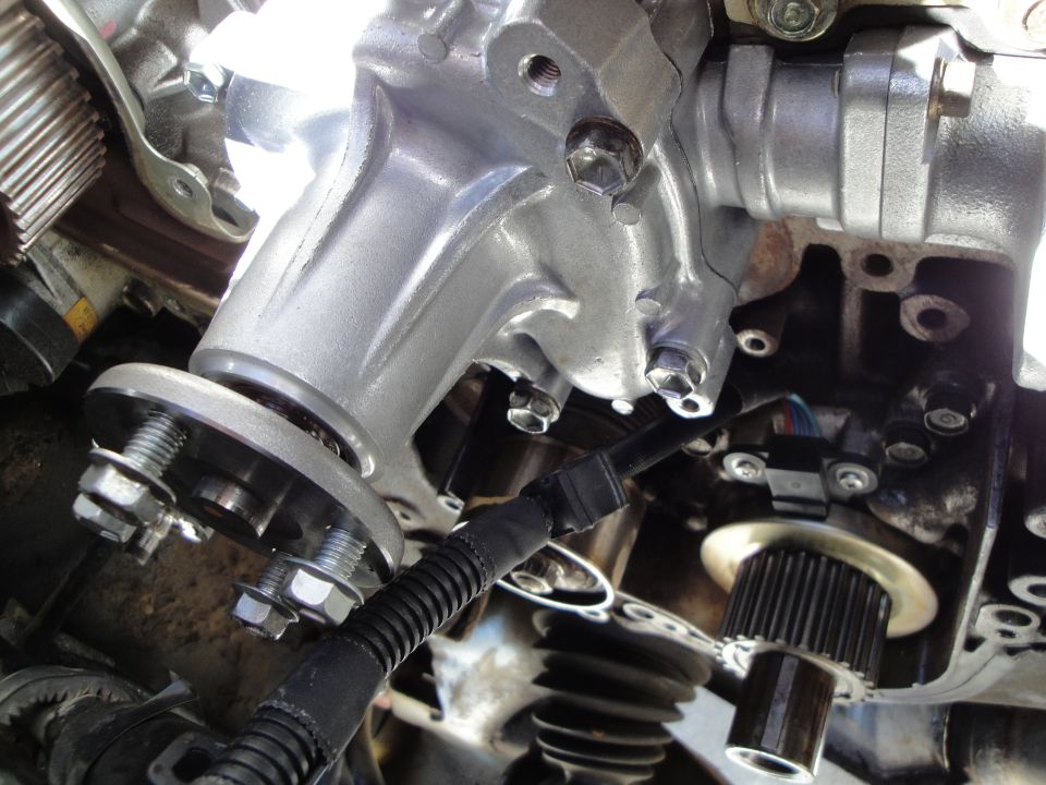 Close-up of a silver metal engine component with bolts and a black wire loom