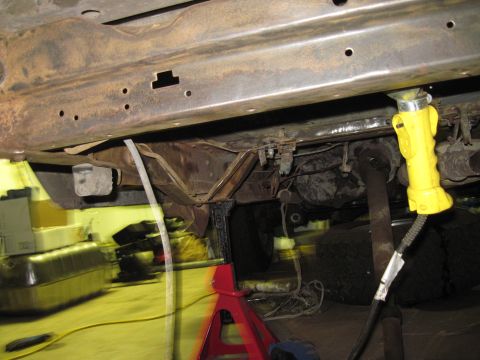 1979 Ford Bronco - The underside of a vehicle is shown, supported by red jack stands and illuminated by a yellow work light, suggesting it is undergoing maint…