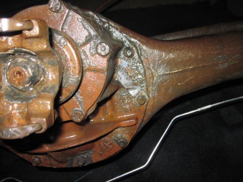 1979 Ford Bronco - Close-up view of a heavily rusted vehicle axle differential, showing bolts and a metal rod.