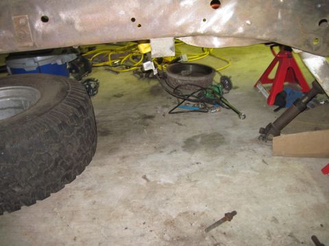 1979 Ford Bronco - The underside of a vehicle is visible, with a tire, tools, and jack stands on the floor.