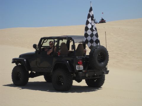 1989 Ford Bronco - Jeep Wrangler driving on sand dunes with a checkered flag flying.