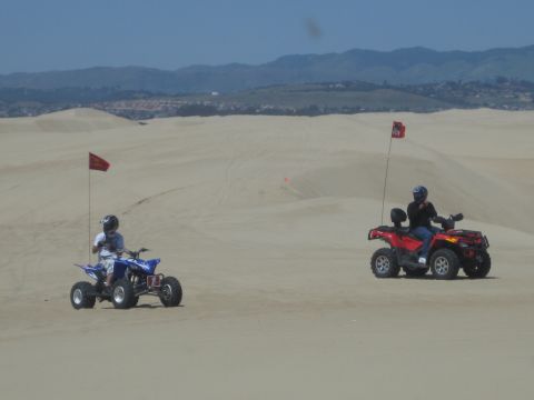 1989 Ford Bronco - Two people ride ATVs across a sandy landscape under a clear blue sky.