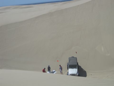 1989 Ford Bronco - People and a Jeep are stopped on a large sand dune under a clear blue sky.