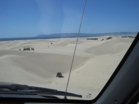 1989 Ford Bronco - Several off-road vehicles are seen traversing sand dunes near the ocean on a clear day.