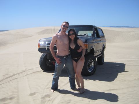1989 Ford Bronco - A couple poses in front of a black 1987 Ford Bronco with lifted suspension on a sandy landscape.