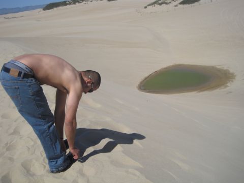 1989 Ford Bronco - Man tying his shoe on a sand dune near a small puddle.