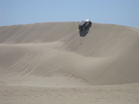 1989 Ford Bronco - A white SUV navigates a steep sand dune under a clear blue sky.
