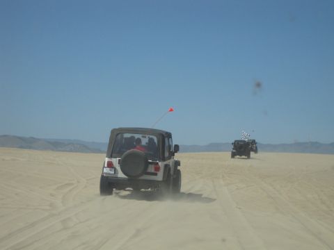 1989 Ford Bronco - Multiple Jeeps traverse sandy terrain under a clear blue sky.