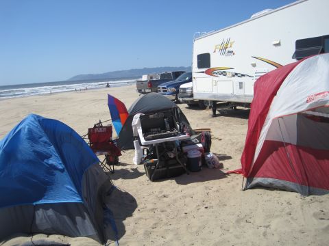 1989 Ford Bronco - Beach camping scene with multiple tents, a stove setup, and RV parked near pickup trucks.