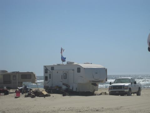 1989 Ford Bronco - Several recreational vehicles and a pickup truck are parked on a beach near the ocean under a clear blue sky.