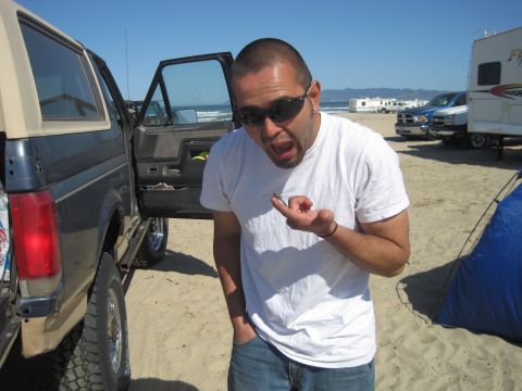 1989 Ford Bronco - A man shows off a small insect he found while camping on the beach with other vehicles nearby.