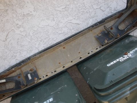 1989 Ford Bronco - A detached vehicle bumper is shown, positioned above two green trash receptacles.
