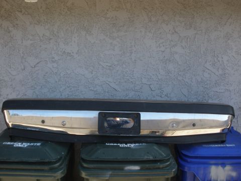 1989 Ford Bronco - A chrome bumper with a license plate mount is shown, resting on top of trash bins.