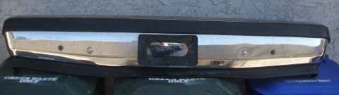 1989 Ford Bronco - A chrome bumper with black trim and a license plate frame is shown, resting on trash bins.