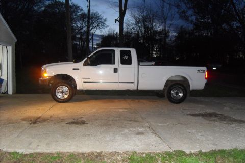 2000 Ford F-250 - A white 2000 Ford F-250 truck is parked on a concrete driveway next to a garage.