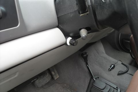 2000 Ford F-250 - Aftermarket knobs installed on the dashboard of a truck, near the steering column and gear shifter.