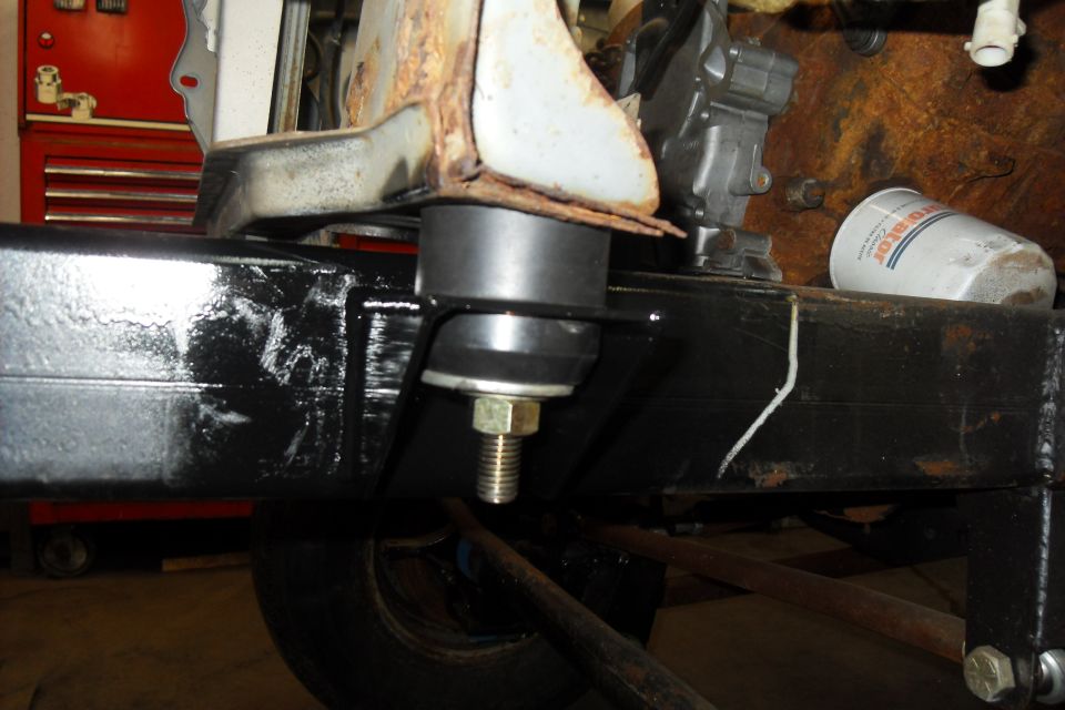 Close-up of a black painted vehicle frame with a rubber mount and bolt. An oil filter is visible in the background