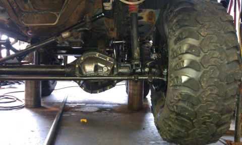 1996 Ford Bronco - A close-up view of the undercarriage of a modified vehicle, highlighting its heavy-duty suspension and large tires.