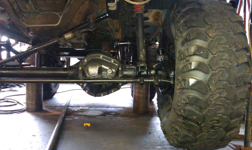 Undercarriage of a lifted vehicle with large off-road tires, showing differential and suspension components