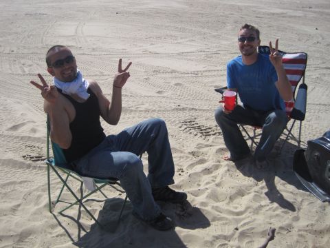 1989 Ford Bronco - Two men relax on a sandy beach, enjoying the day and giving peace signs.