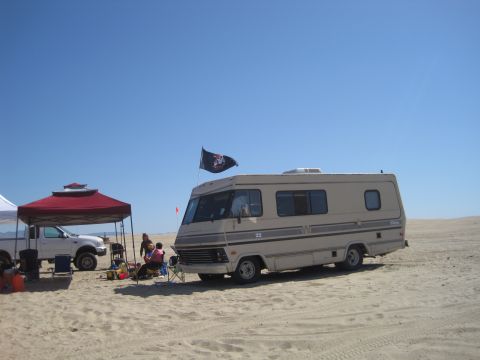 1989 Ford Bronco - A motorhome and a pickup truck are parked on a sandy beach under a clear blue sky.