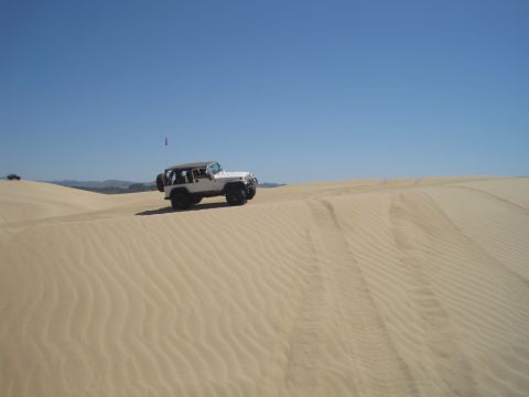 1989 Ford Bronco - A white Jeep navigates the sandy terrain under a clear blue sky.