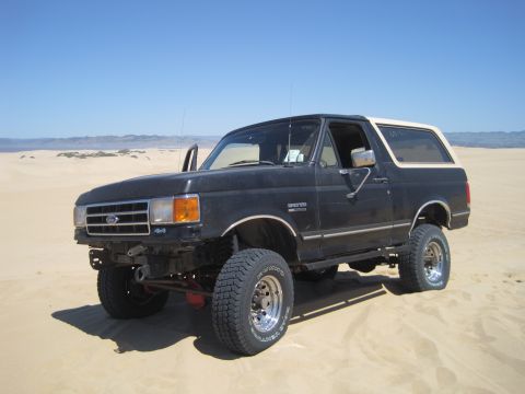 1989 Ford Bronco - This Ford Bronco is parked on a sandy terrain under a clear blue sky.