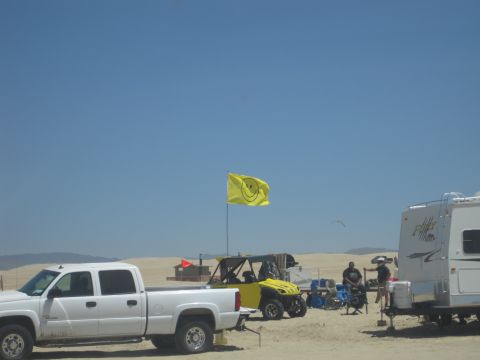 1989 Ford Bronco - A yellow UTV flies a smiley face flag in a sandy recreational area, accompanied by a pickup truck and an RV.
