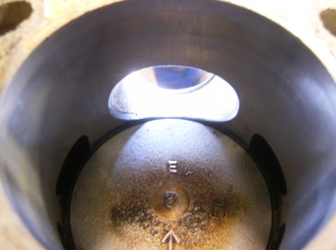 2000 Ford E350 - Close-up looking straight down a two-stroke cylinder bore at the piston crown, with the exhaust port opening visible in the bore wall and t…