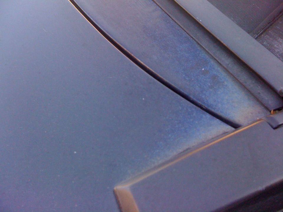 Close-up of a dark blue car hood with a seam and some dust