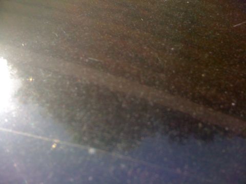 1985 Ford Mustang - Close-up of a dark, reflective surface, possibly a car's paint, showing scratches and light glare.