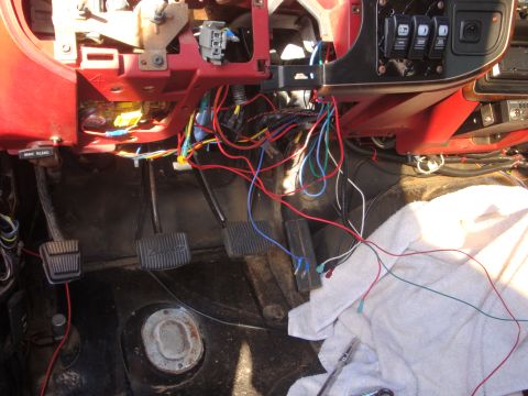 1989 Ford Bronco - The dashboard and floor of a vehicle are shown with a complex and messy wiring harness exposed.