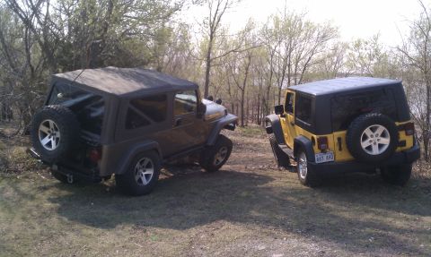 2005 Jeep Wrangler - Two Jeep Wranglers are parked on a dirt path surrounded by trees and foliage.