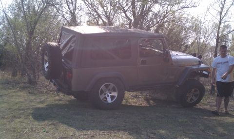 2005 Jeep Wrangler - A brown Jeep Wrangler is parked outdoors on a grassy area, with a man standing nearby.