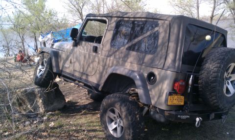 2005 Jeep Wrangler - A Jeep Wrangler is positioned on rocks near a body of water, with a spare tire mounted on the rear.