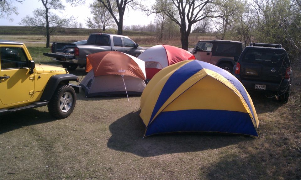 Yellow Jeep Wrangler Rubicon and other vehicles parked behind dome tents at a grassy campsite