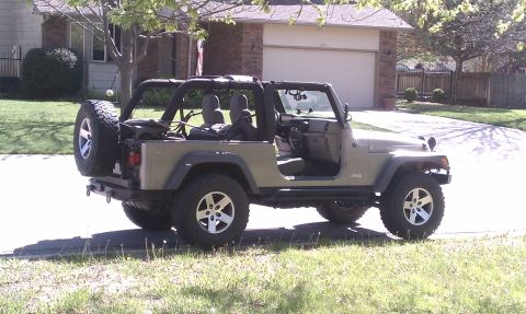 2005 Jeep Wrangler - Khaki Jeep Wrangler Unlimited Rubicon parked in a suburban driveway, seen from the rear three-quarter with doors and top removed, showing t…