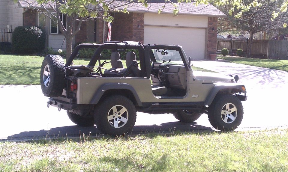 Khaki Jeep Wrangler Unlimited Rubicon with doors and top off, parked in a suburban driveway