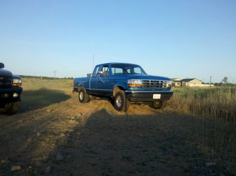 1992 Ford F-150 - A blue 1992 Ford F-150 pickup truck is parked outdoors in a grassy field under a clear sky.