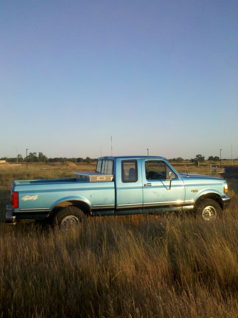 1992 Ford F-150 - A light blue 1992 Ford F-150 pickup truck sits in a field of tall grass under a clear blue sky.