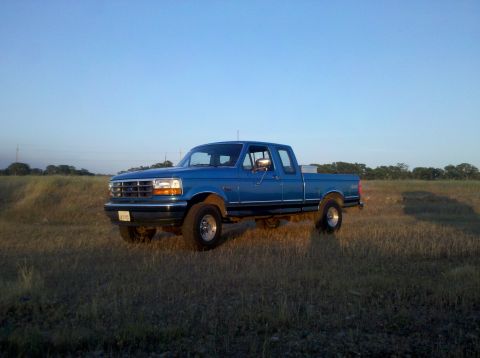 1992 Ford F-150 - A blue 1992 Ford F-150 pickup truck is seen from a three-quarter front view in a field under a clear sky.